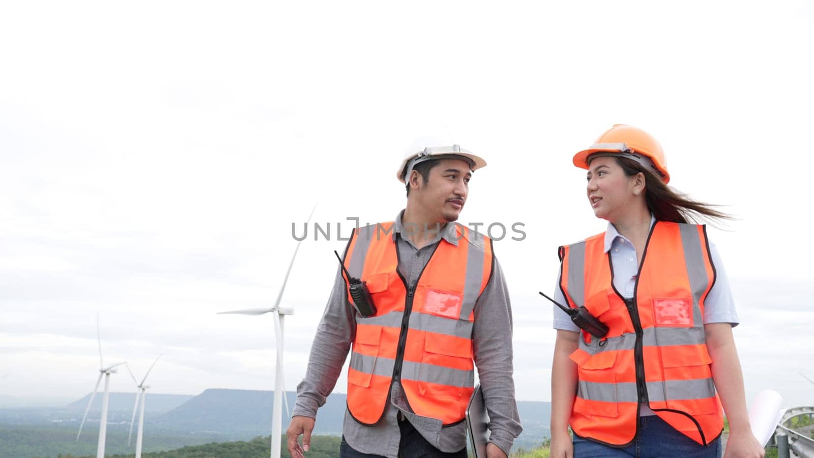 Male and female engineers working on a wind farm atop a hill or mountain in the rural. Progressive ideal for the future production of renewable, sustainable energy.