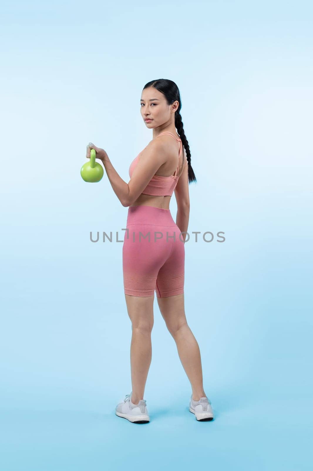 Vigorous energetic woman doing kettlebell weight lifting exercise on isolated background. Young athletic asian woman strength and endurance training session as body workout routine.