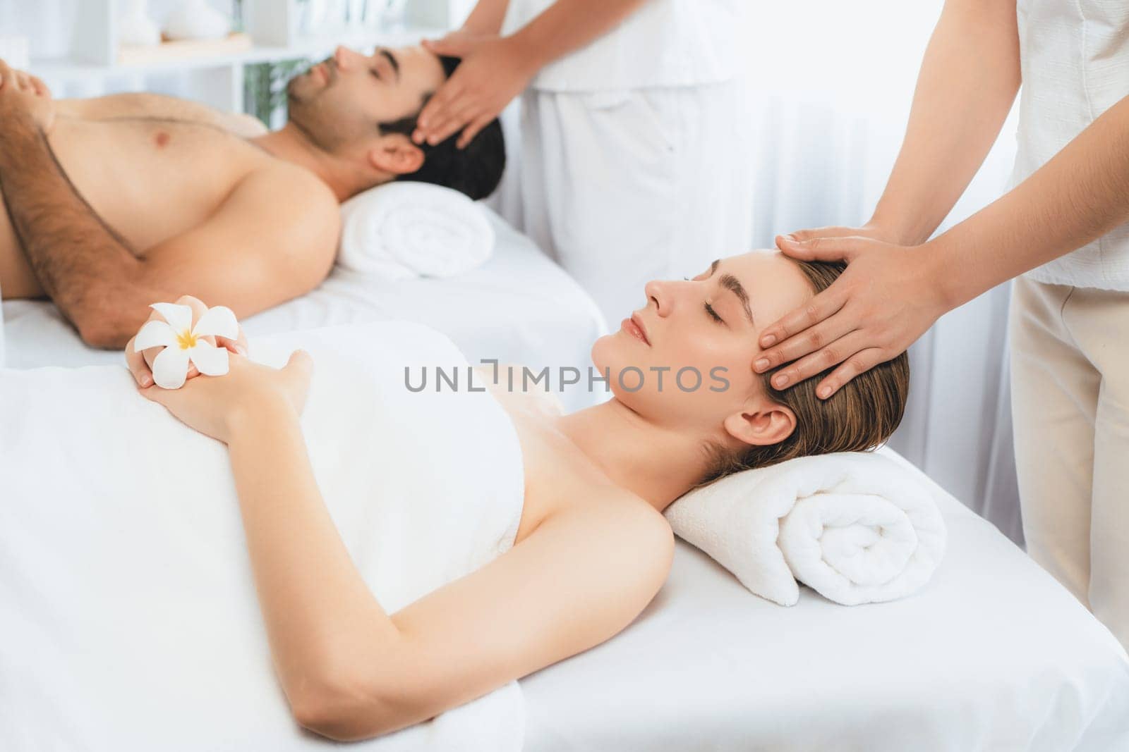 Caucasian couple enjoying relaxing anti-stress head massage and pampering facial beauty skin recreation leisure in dayspa modern light ambient at luxury resort or hotel spa salon. Quiescent