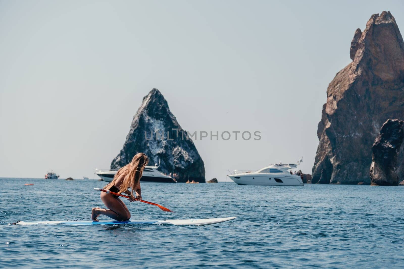 Close up shot of beautiful young caucasian woman with black hair and freckles looking at camera and smiling. Cute woman portrait in a pink bikini posing on a volcanic rock high above the sea