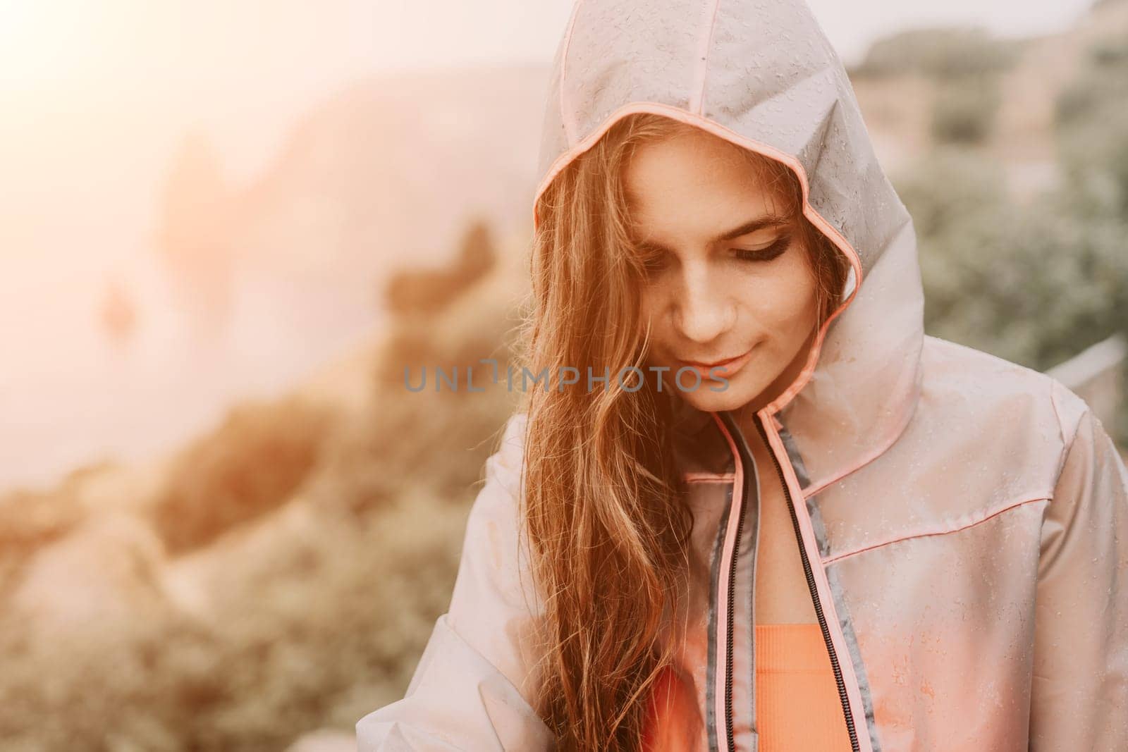 Woman rain park. Happy woman portrait wearing a raincoat with transparent umbrella outdoors on rainy day in park near sea. Girl on the nature on rainy overcast day