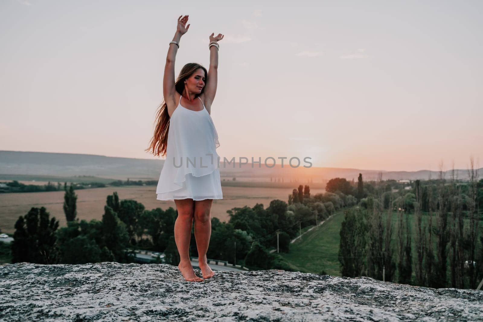 Romantic beautiful bride in white dress posing with sea and mountains in background. Stylish bride standing back on beautiful landscape of sea and mountains on sunset