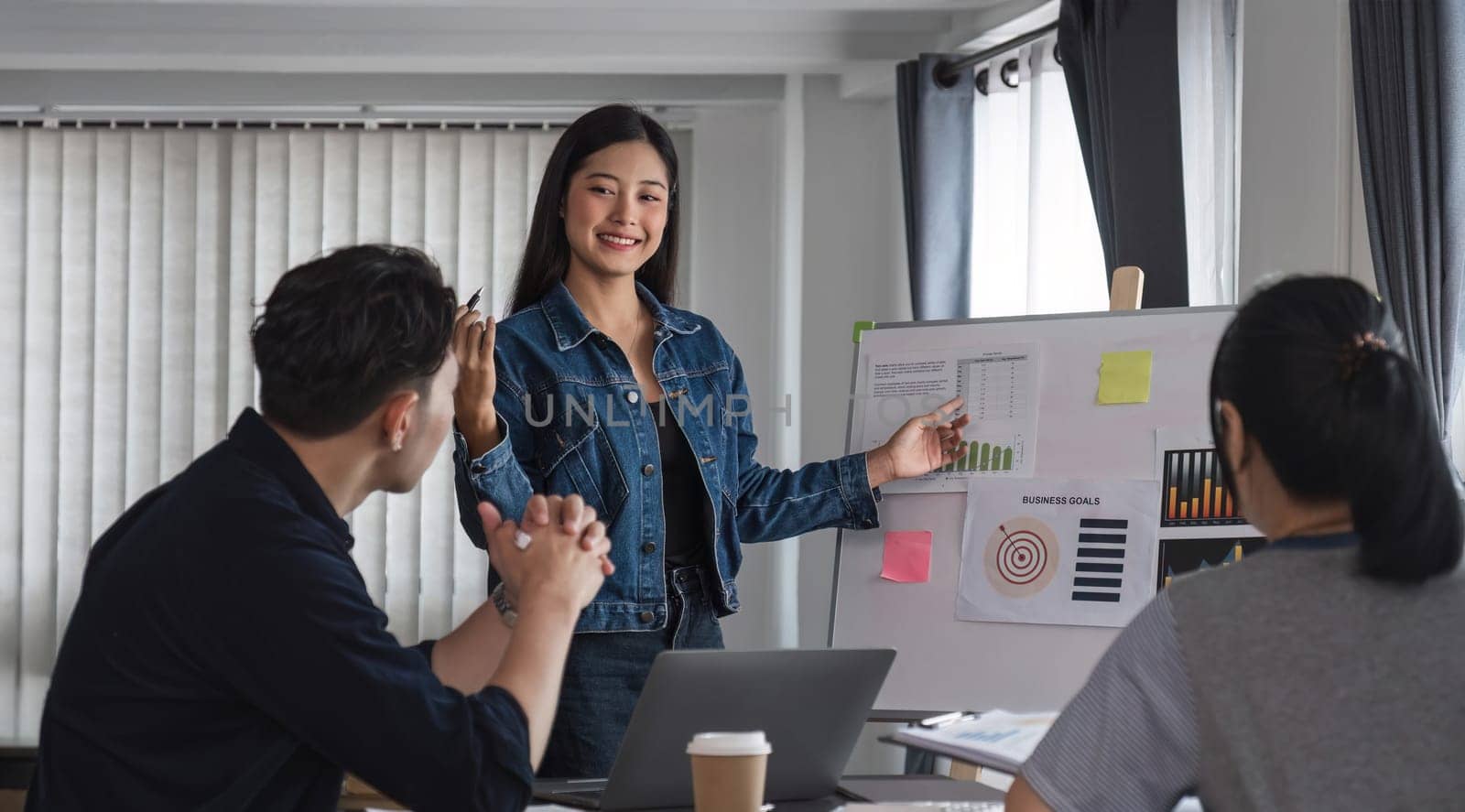 Young businesswoman explains work plan in meeting to teammates in conference room.