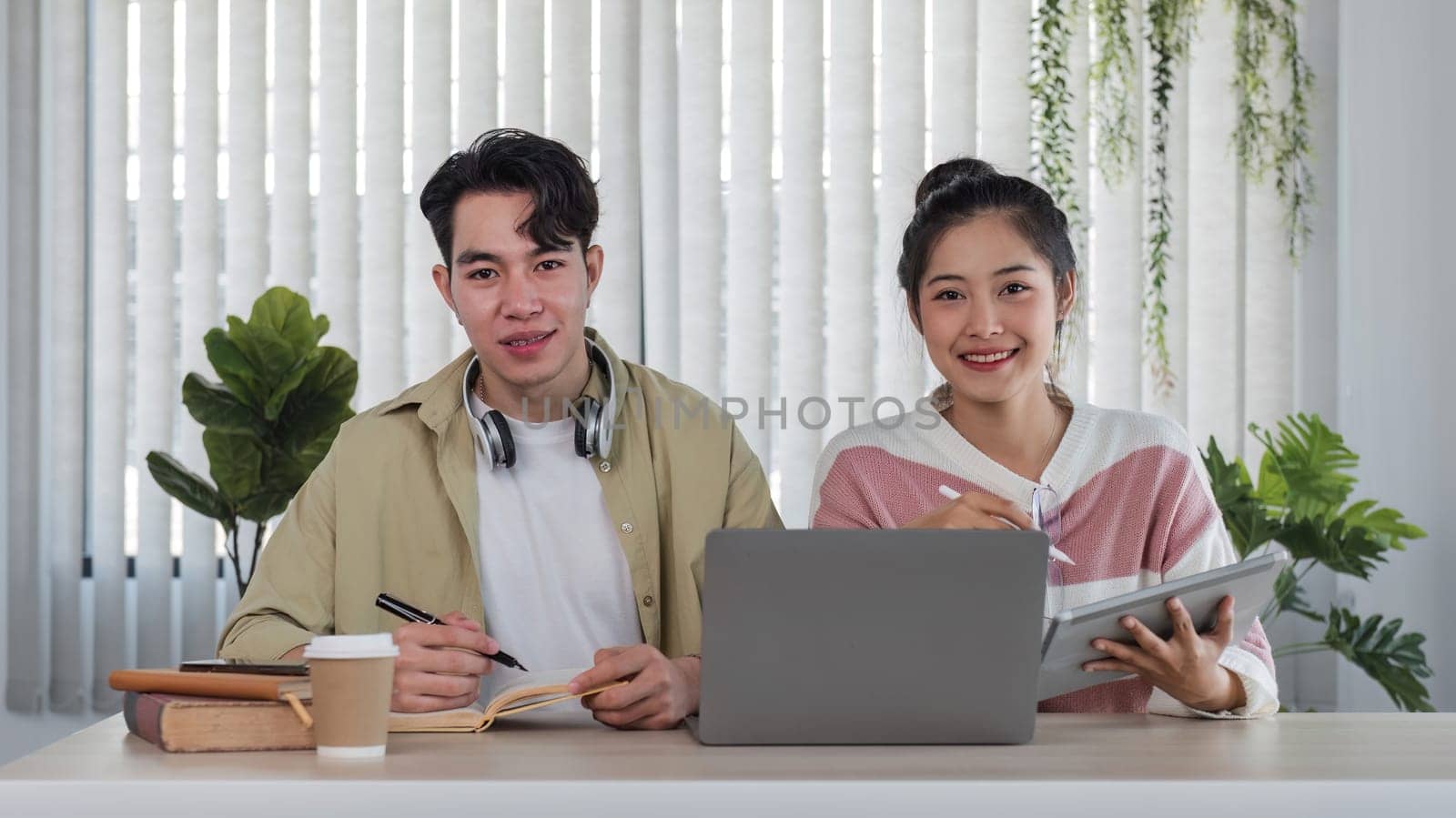 A young man and woman study together online using a video call program on a laptop in the living room. by wichayada