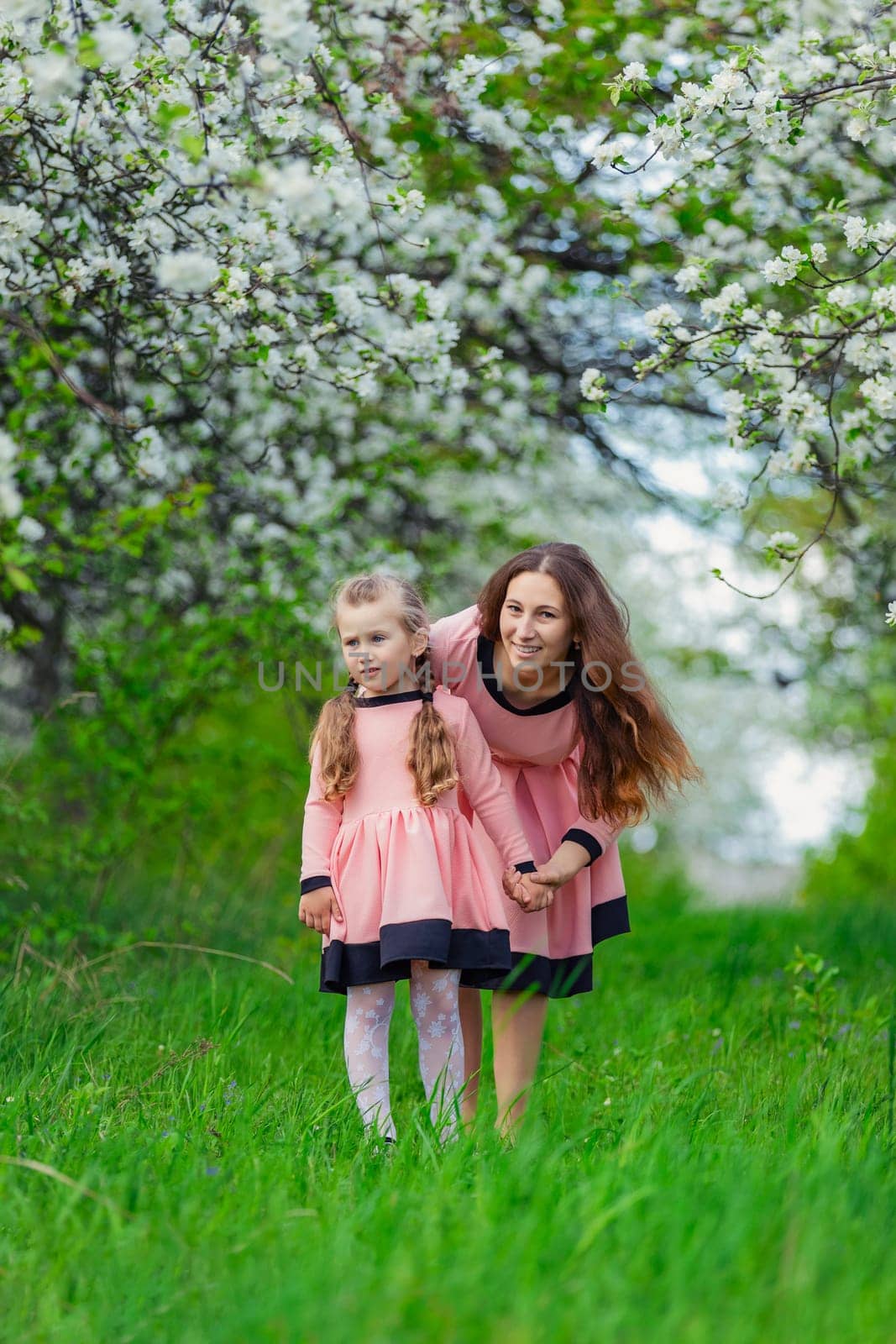 mother and daughter walk through a blooming apple orchard