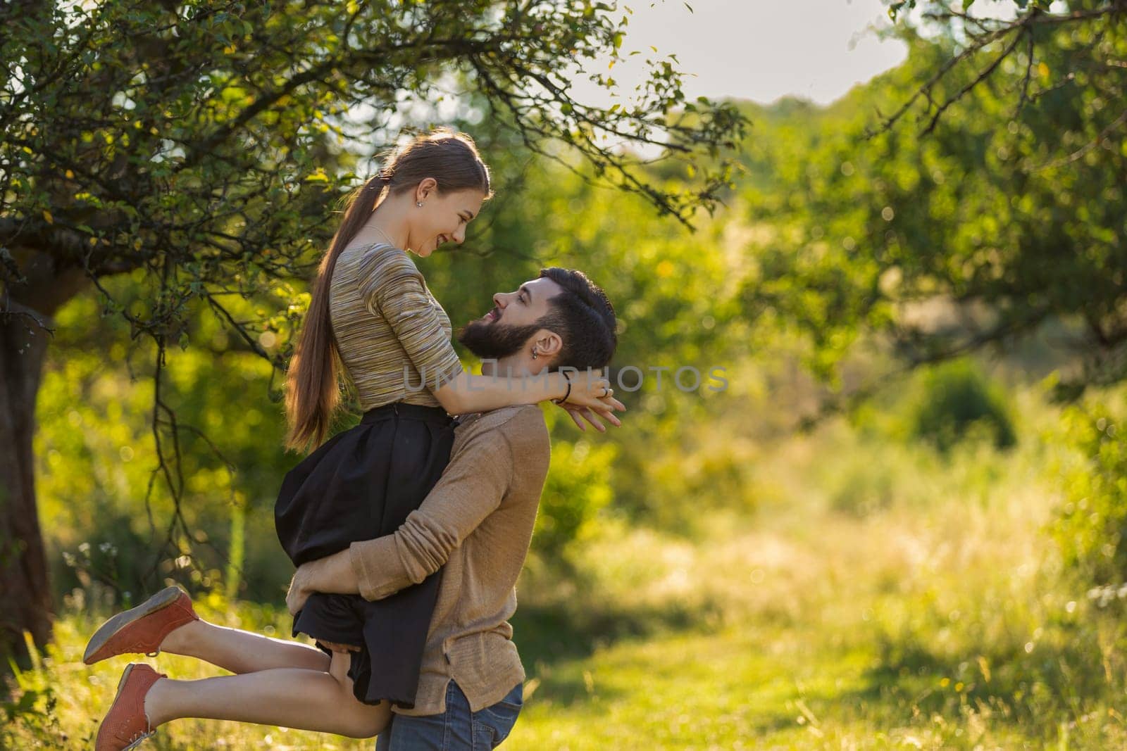 guy carries his girlfriend in his arms in a summer park