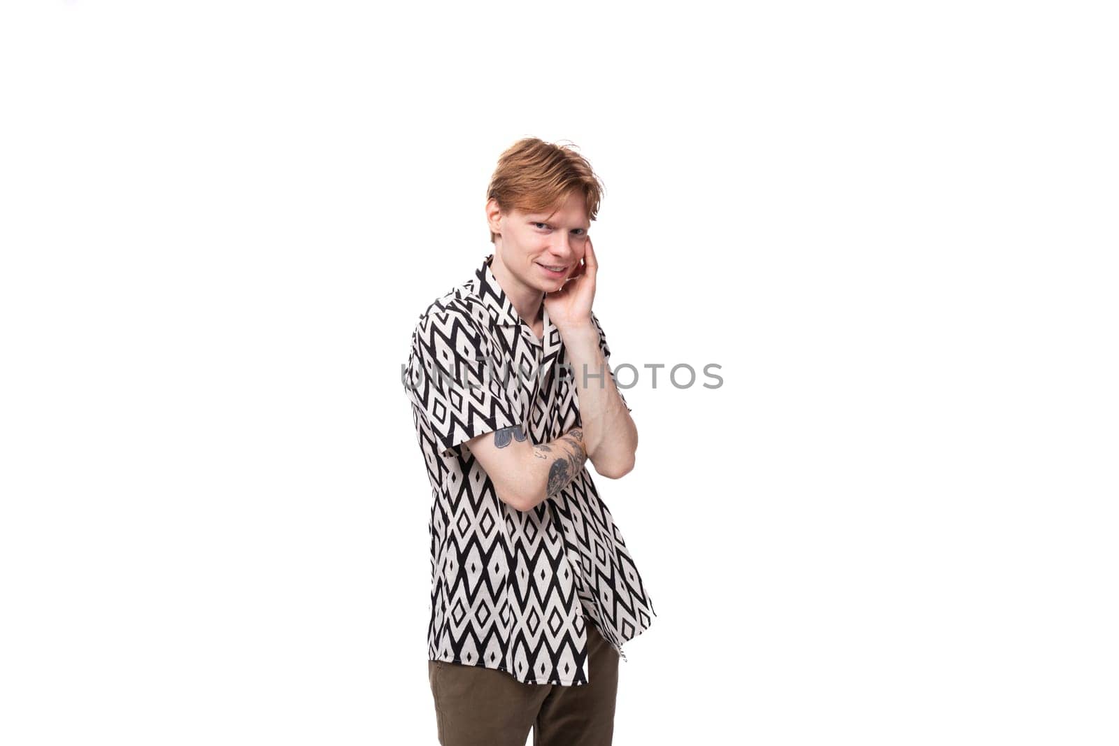 young tired caucasian man with red hair with a tattoo is dressed in a summer black and white shirt on a background with copy space by TRMK