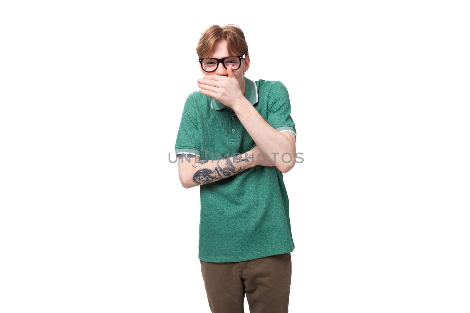 young caucasian man with red hair dressed in a green t-shirt laughs with his mouth closed on the background with copy space.