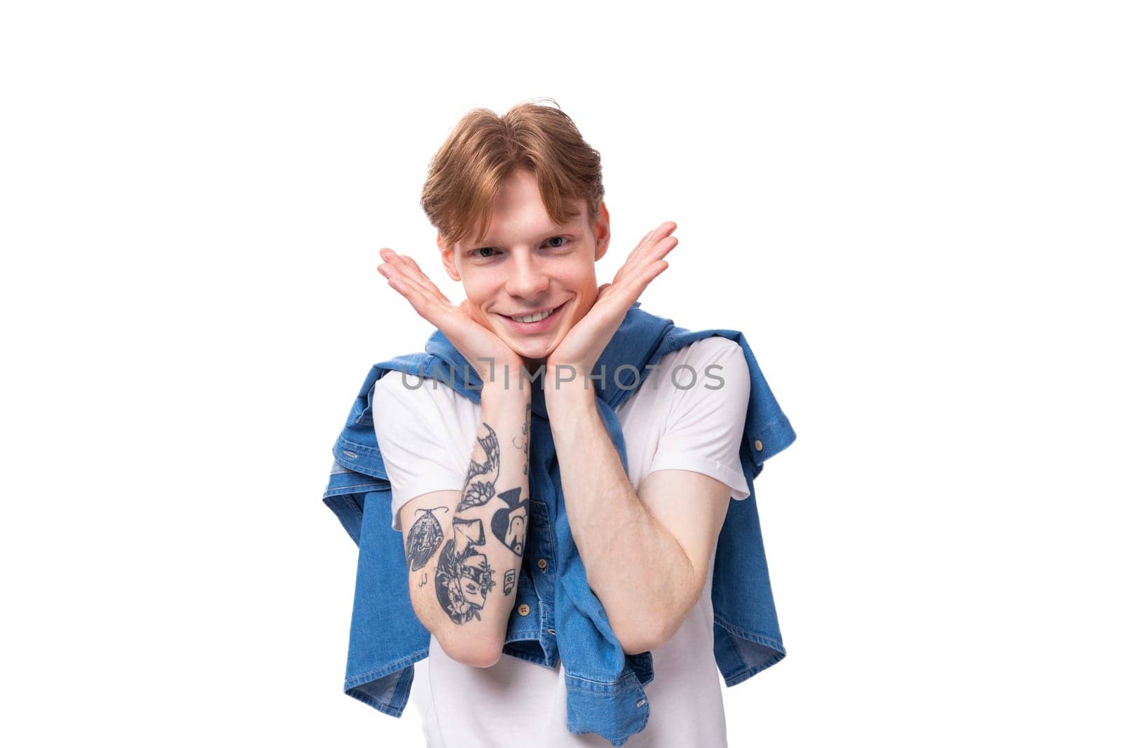 young short-haired caucasian male student with golden red hair with a tattoo on his arms is dressed in a white t-shirt.