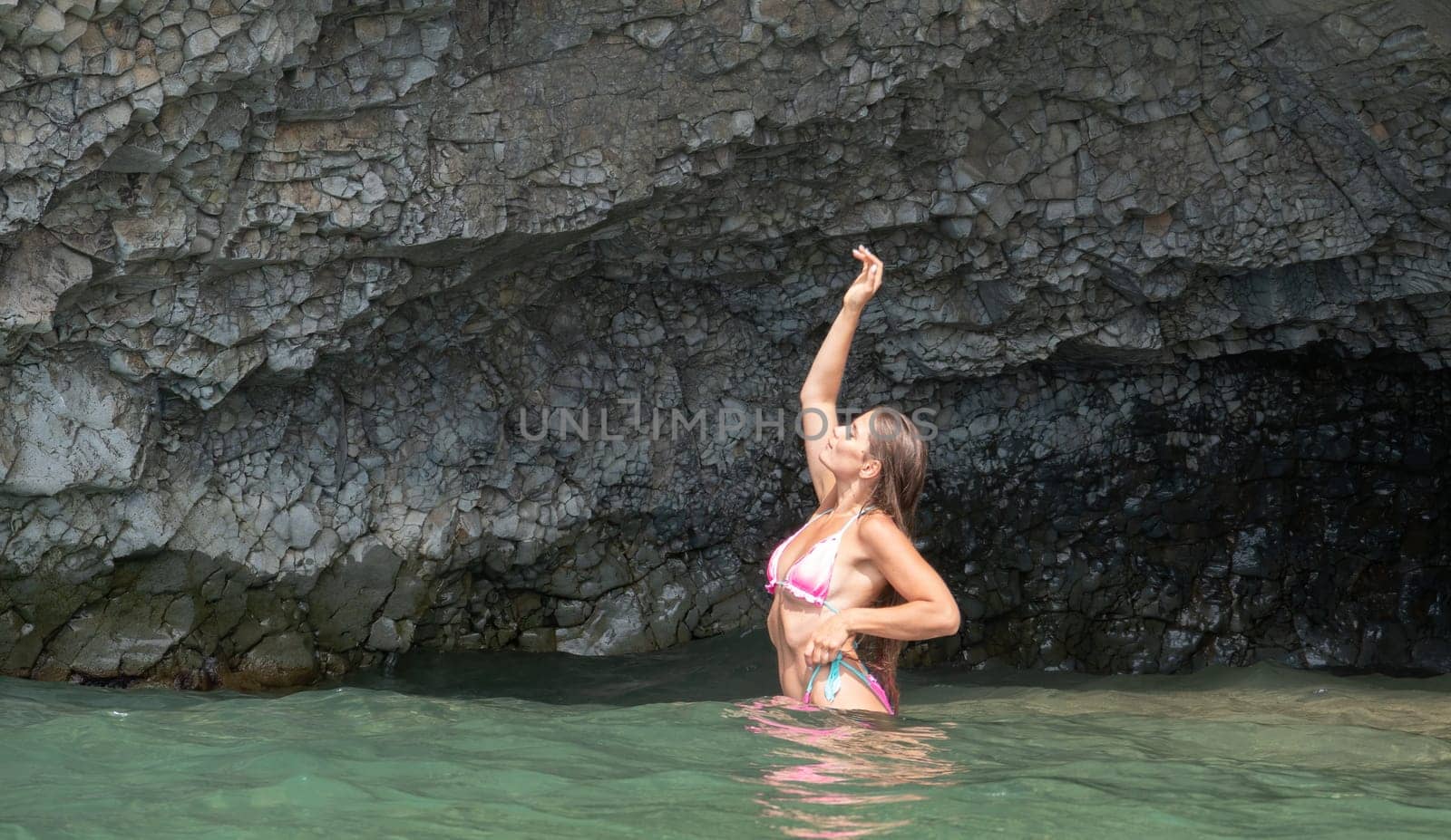 Woman travel sea. Happy Woman traveler shares adventure journey at sea, surrounded by volcanic mountains on beach. Happy tourist captures memory in pink bikini. by panophotograph