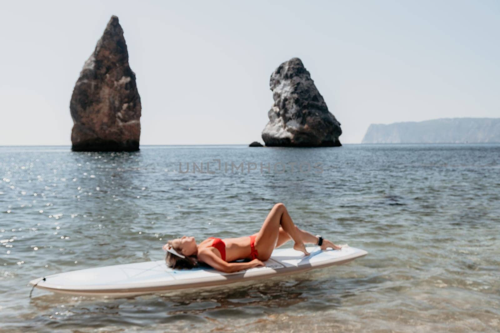 Close up shot of beautiful young caucasian woman with black hair and freckles looking at camera and smiling. Cute woman portrait in a pink bikini posing on a volcanic rock high above the sea