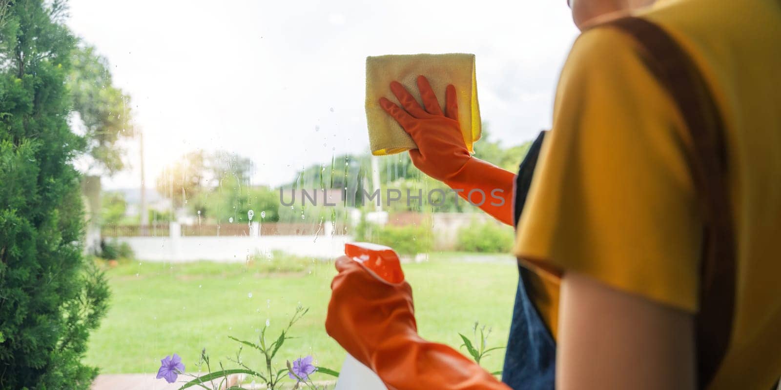 Young Asian housewife cleaning window glass with rags and detergent spray, cleaning house on the weekend.