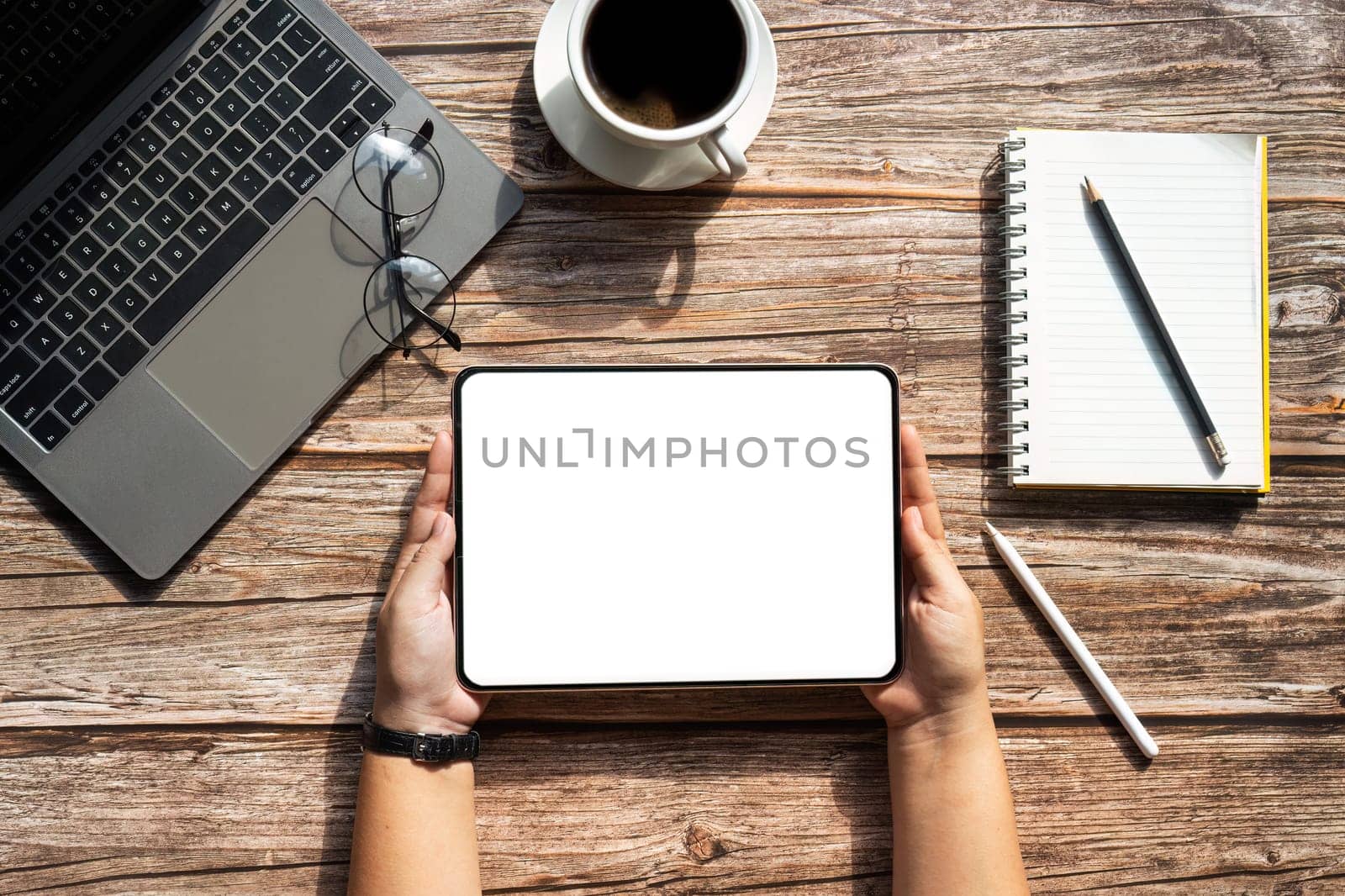 Top view tablet that someone is holding with blank screen mock up digital tablet on workspace office desk with cup of coffee, notebook and laptop by nateemee