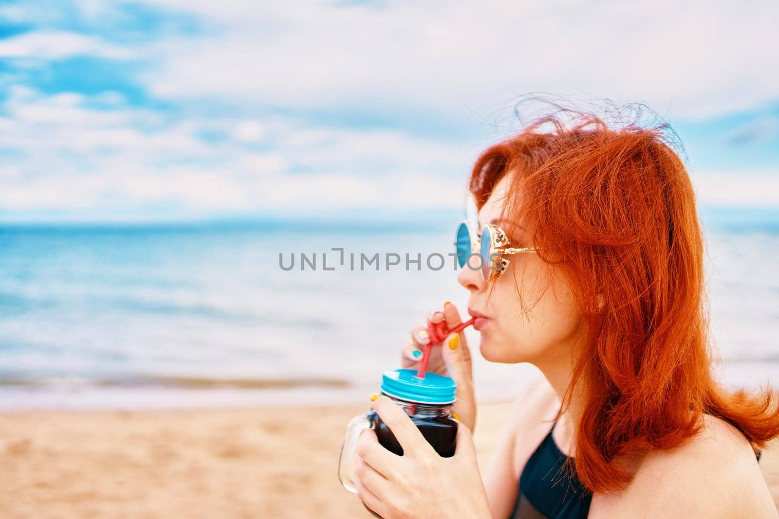 A woman is savoring a refreshing cold drink at the beach, fully embracing relaxation and the sunny atmosphere