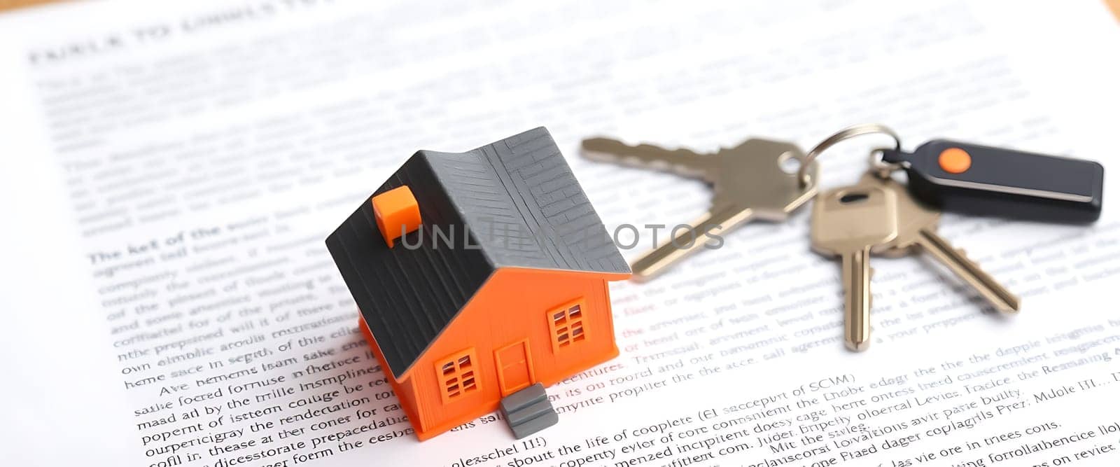 A small orange house model sits beside keys on a pile of printed documents related to real estate, highlighting the process of purchasing a new home.