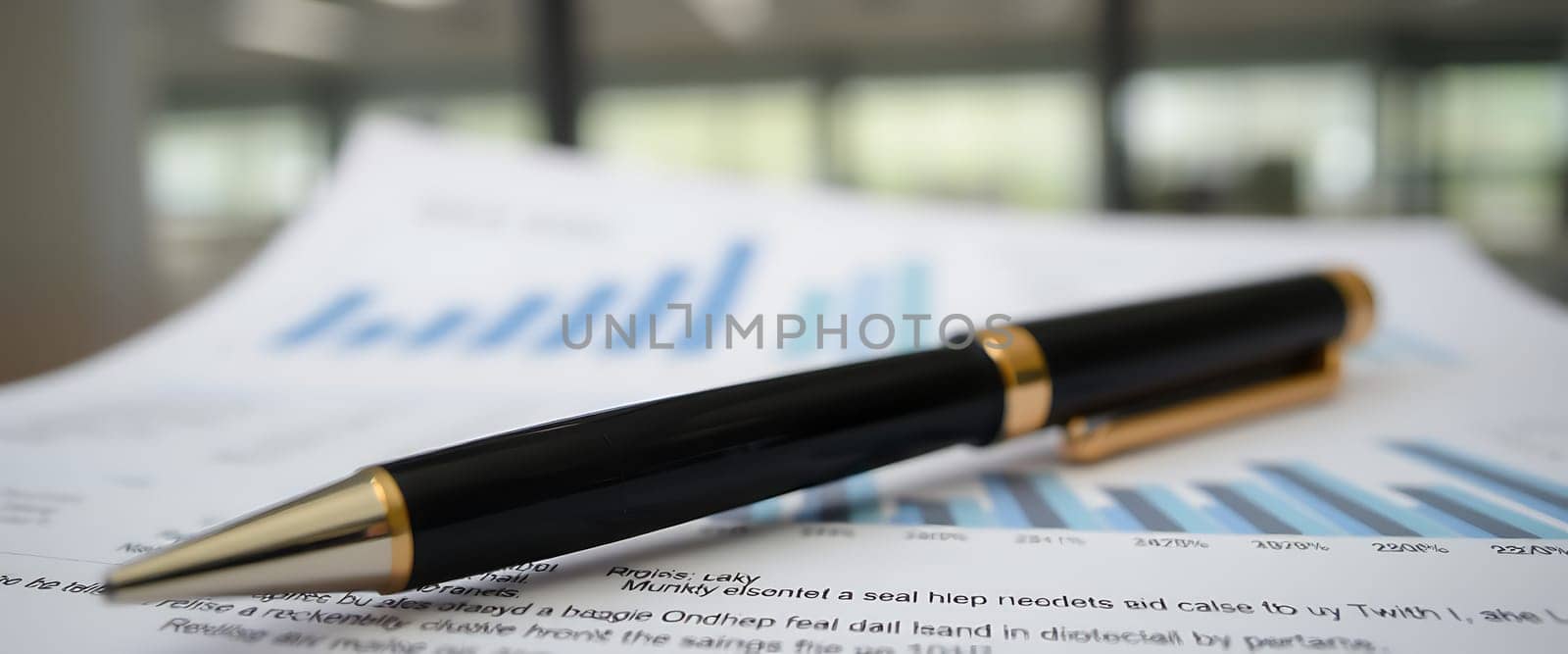 A sleek black pen placed atop a set of financial documents showcasing bar graphs and data analysis, reflecting an active business discussion.