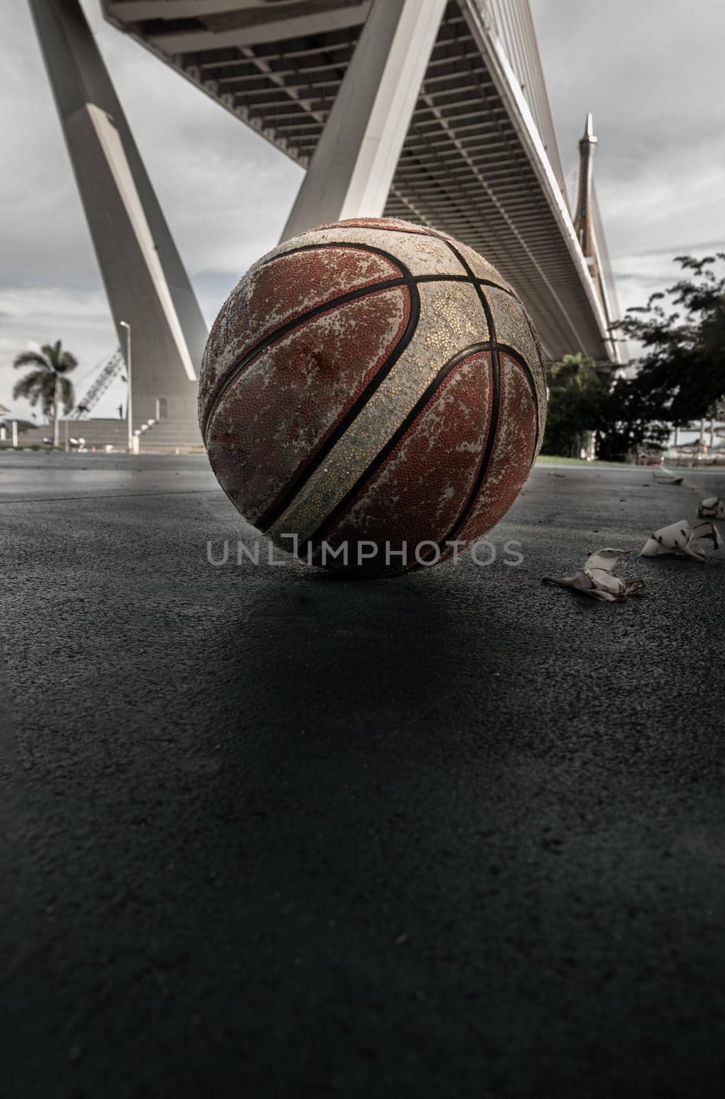 Basketball ball on the Old cement court floor at Outdoor park with Suspension bridge and Sky in the background. Space for text, Selective focus.