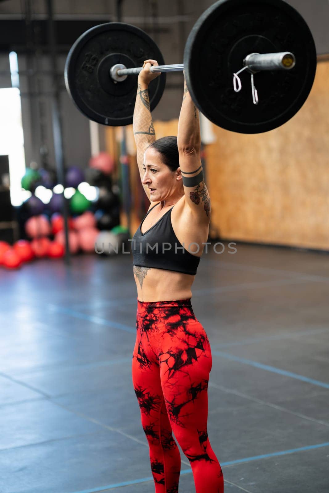 Vertical photo of a mature sportive and strong woman lifting weights alone in a gym