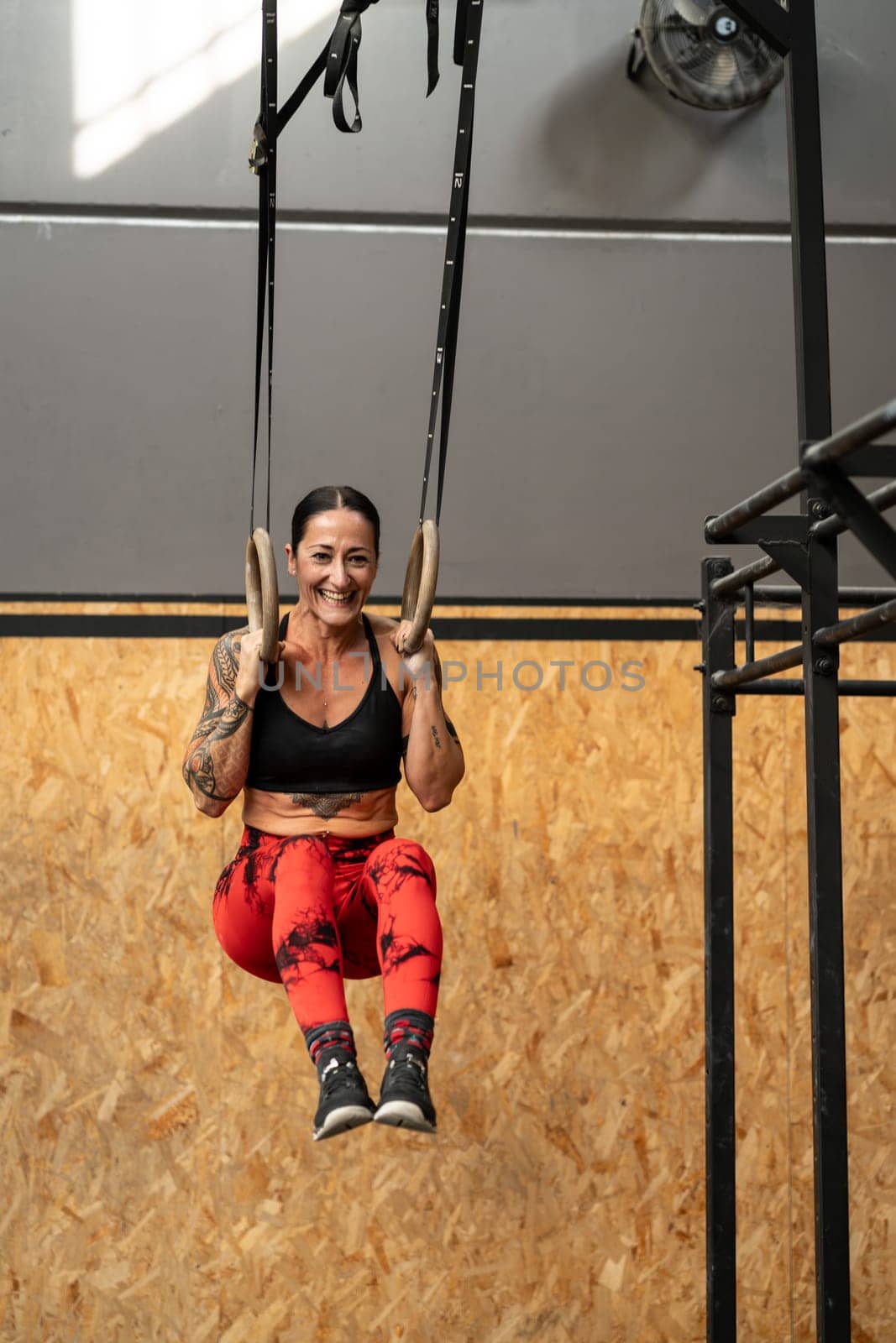 Vertical photo of a happy sportive woman training with rings in a cross training gym