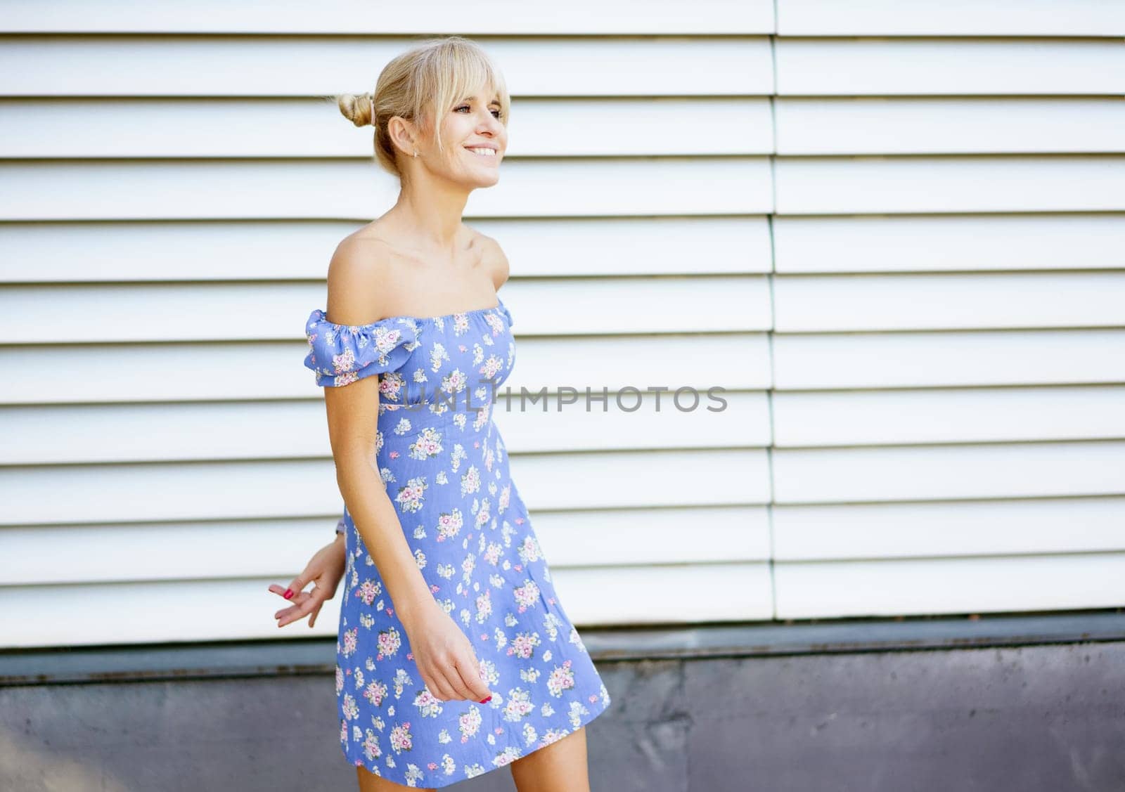 Horizontal photo three quarter length side view of a blonde woman in summer dress standing dancing in the city