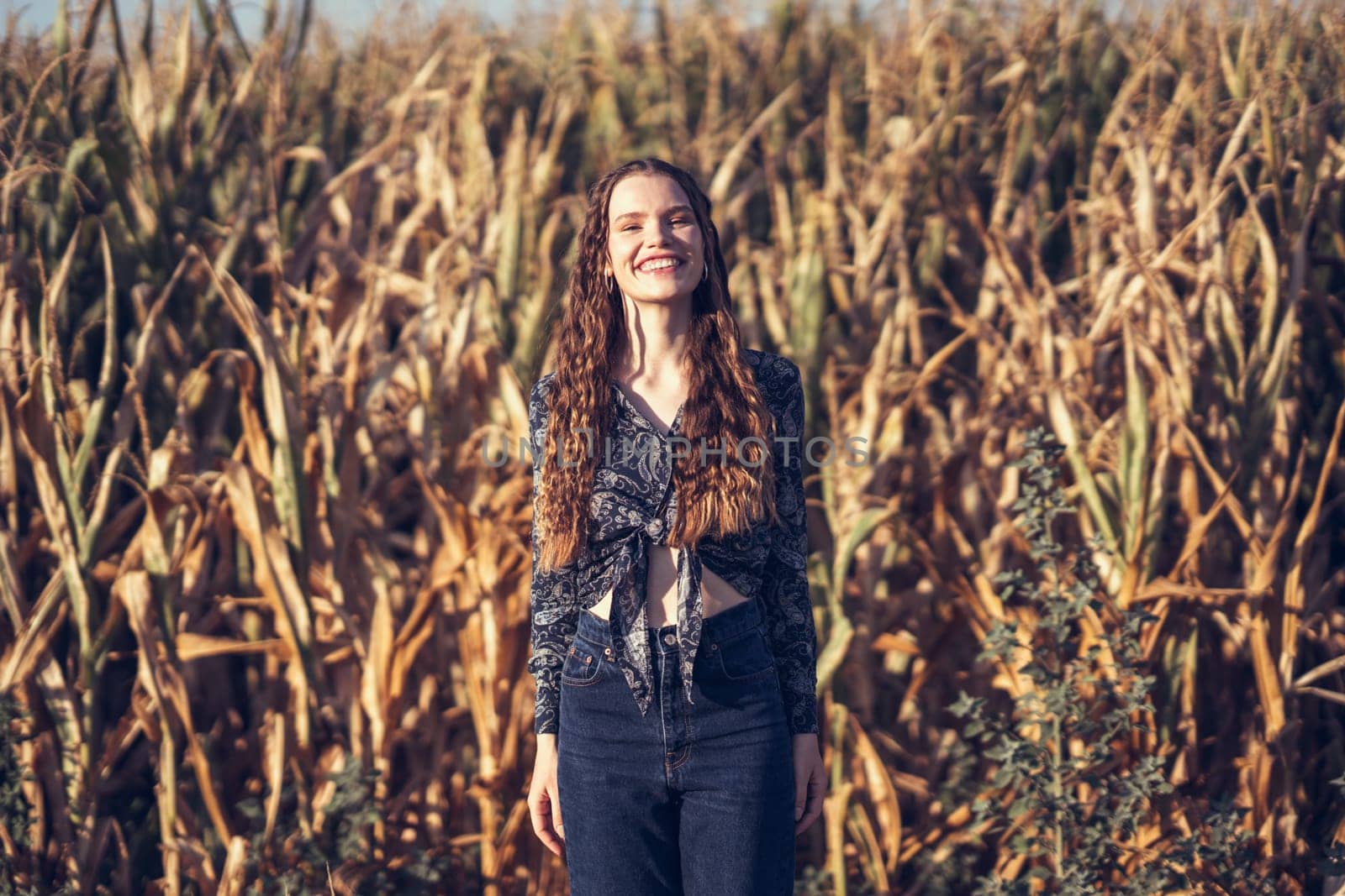 A joyful young woman beams brightly as she stands amidst a lush golden cornfield, perfectly capturing the essence of rural beauty along with the blissful, carefree moments that we truly cherish