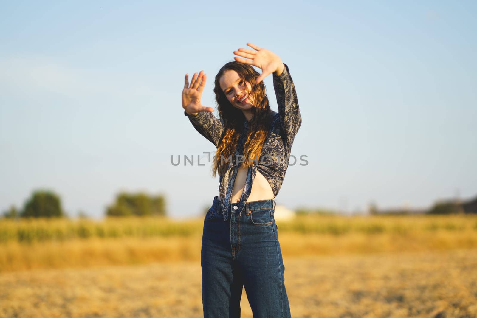 A cheerful young woman joyfully strikes a playful pose in a sunlit field, perfectly capturing the essence of summer, joy, spontaneity, and the feeling of unrestricted freedom that comes with it