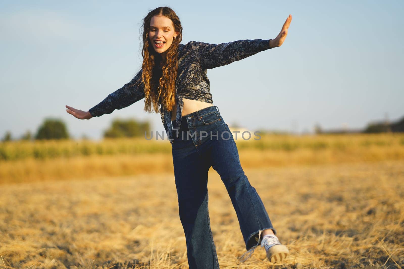 In a vibrant golden field, a joyful young woman dances with exuberance, embodying the spirit of freedom and happiness as she moves gracefully beneath the vast expanse of a clear blue sky