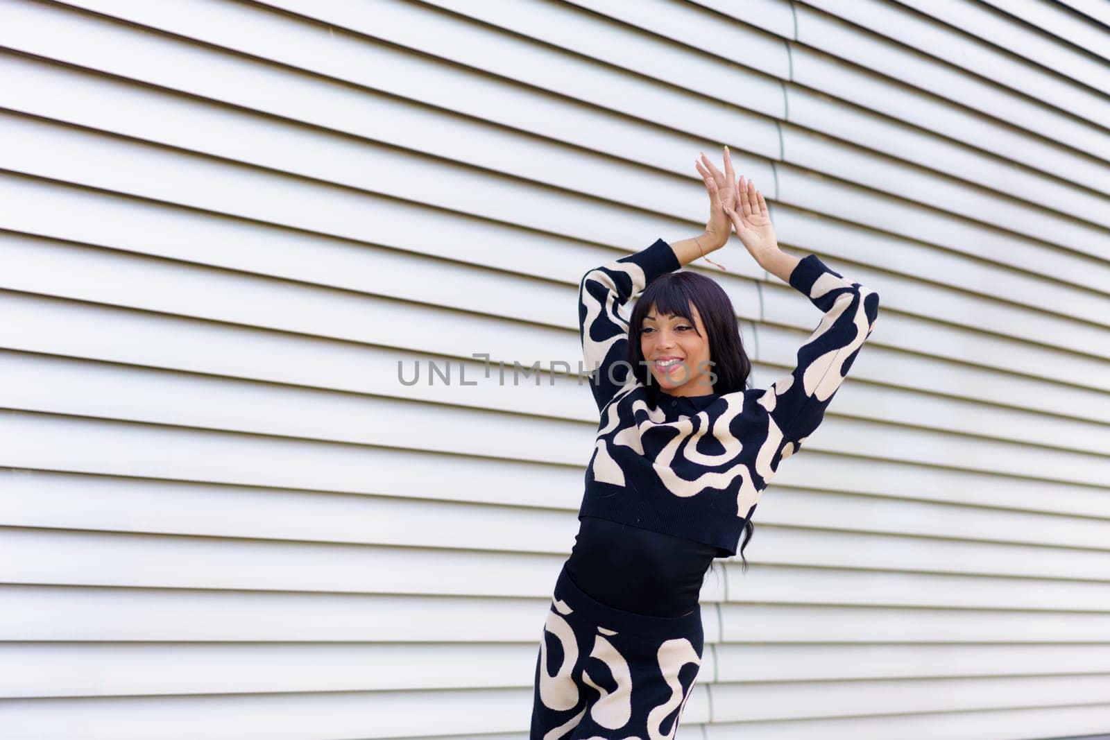 Happy beauty female dancer with modern clothes raising hands posing on the street in a urban space