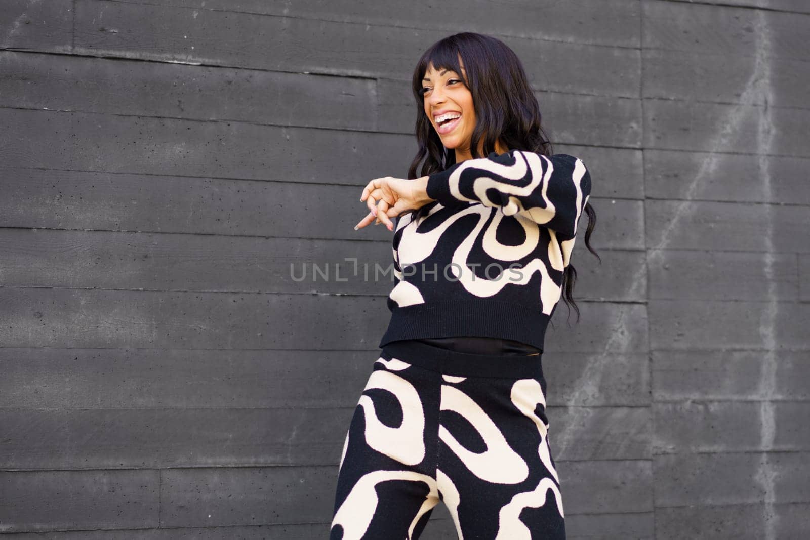 Three quarter length photo of a hispanic adult female smiling dancer performing in the street next to grey wall