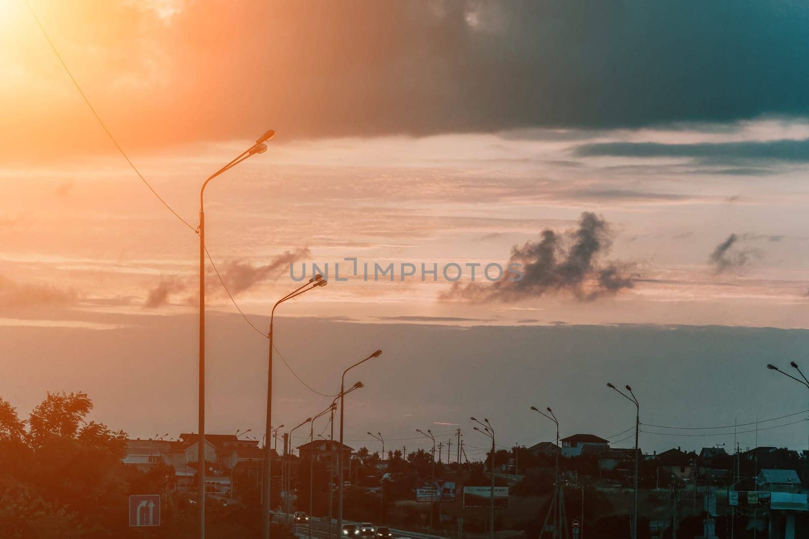 A sky with a few clouds and a street with a few street lights. The sky is a mix of blue and orange