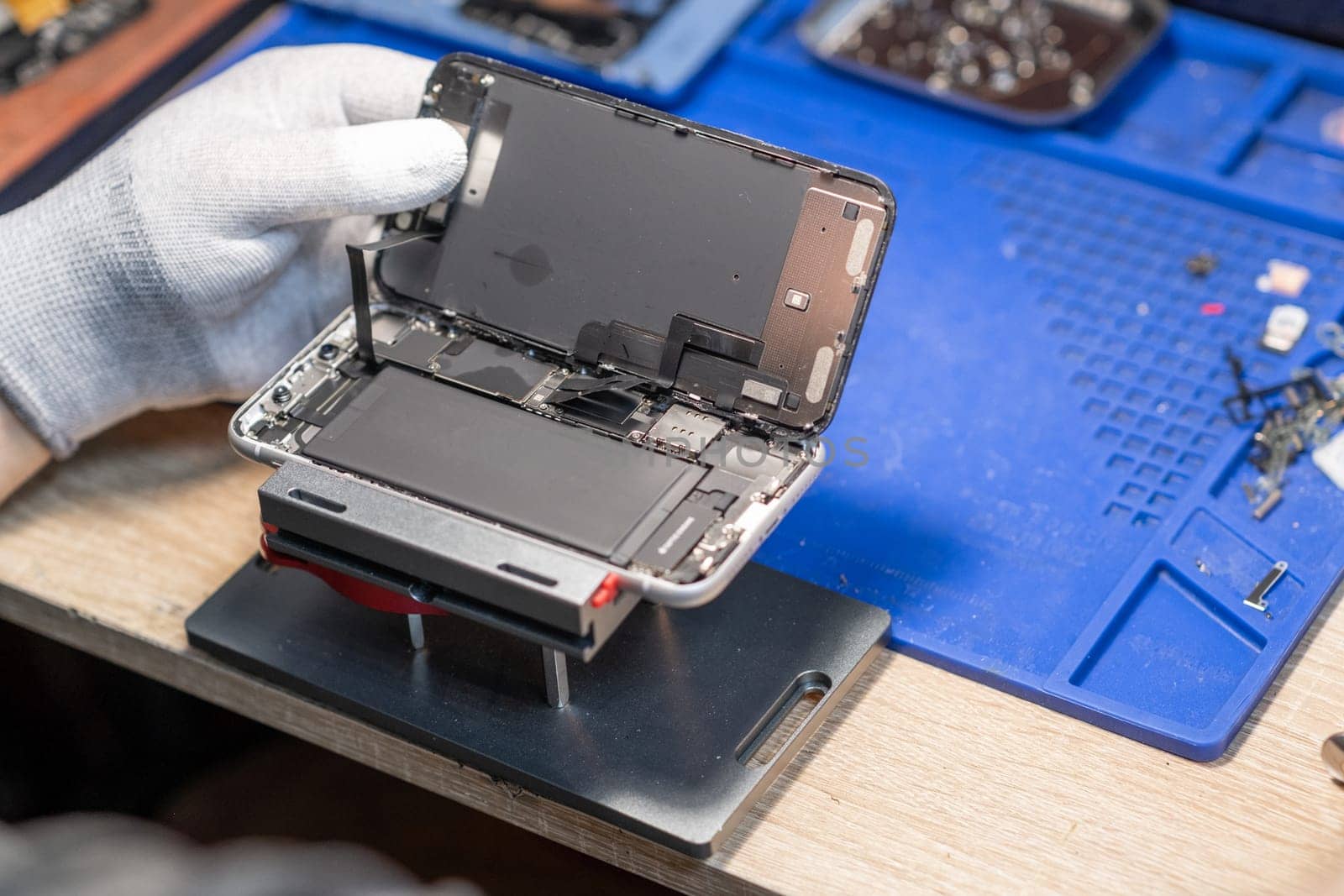 A technician performs a battery replacement on a mobile device, showcasing tools and parts in a well-organized repair workspace.
