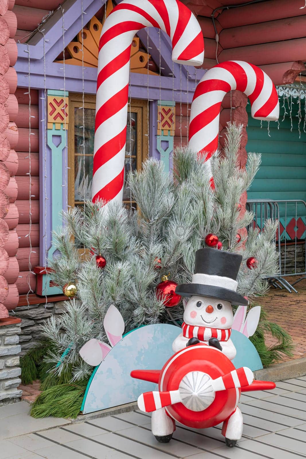 A cheerful snowman with a red and white striped scarf sits beside large candy canes and festive greenery, creating a joyful holiday atmosphere in a vibrant setting.