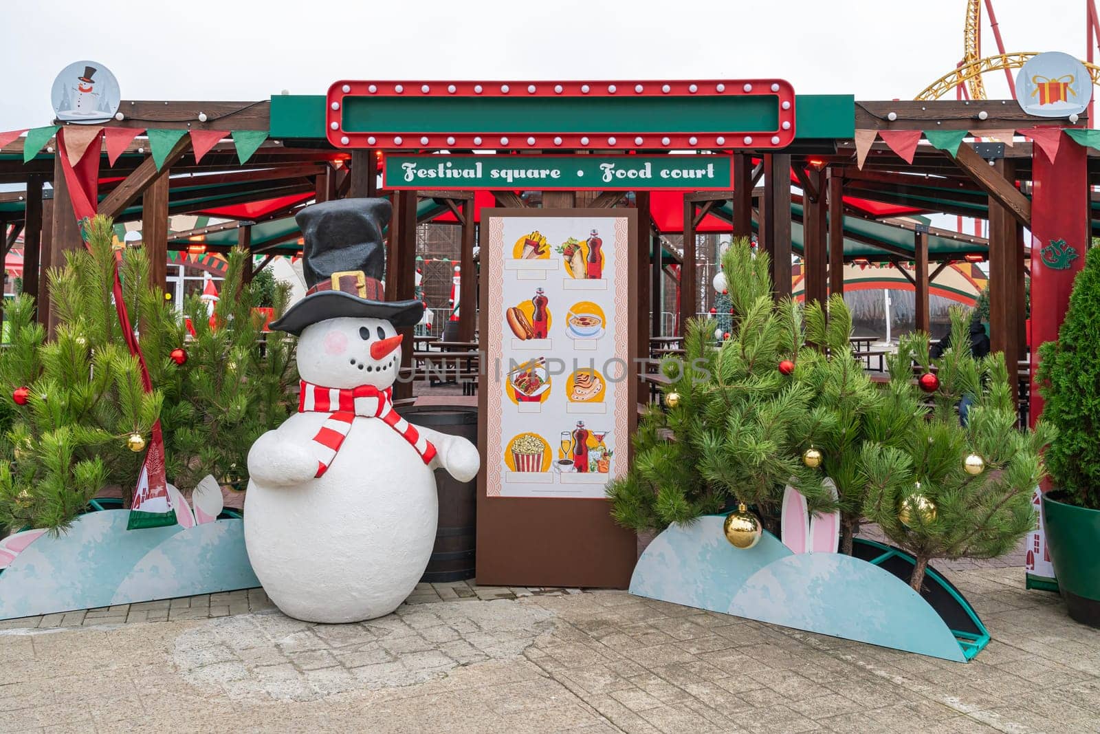 A cheerful snowman stands in a vibrant food court area of a winter festival, surrounded by evergreen trees and festive decorations, inviting visitors to enjoy seasonal treats.