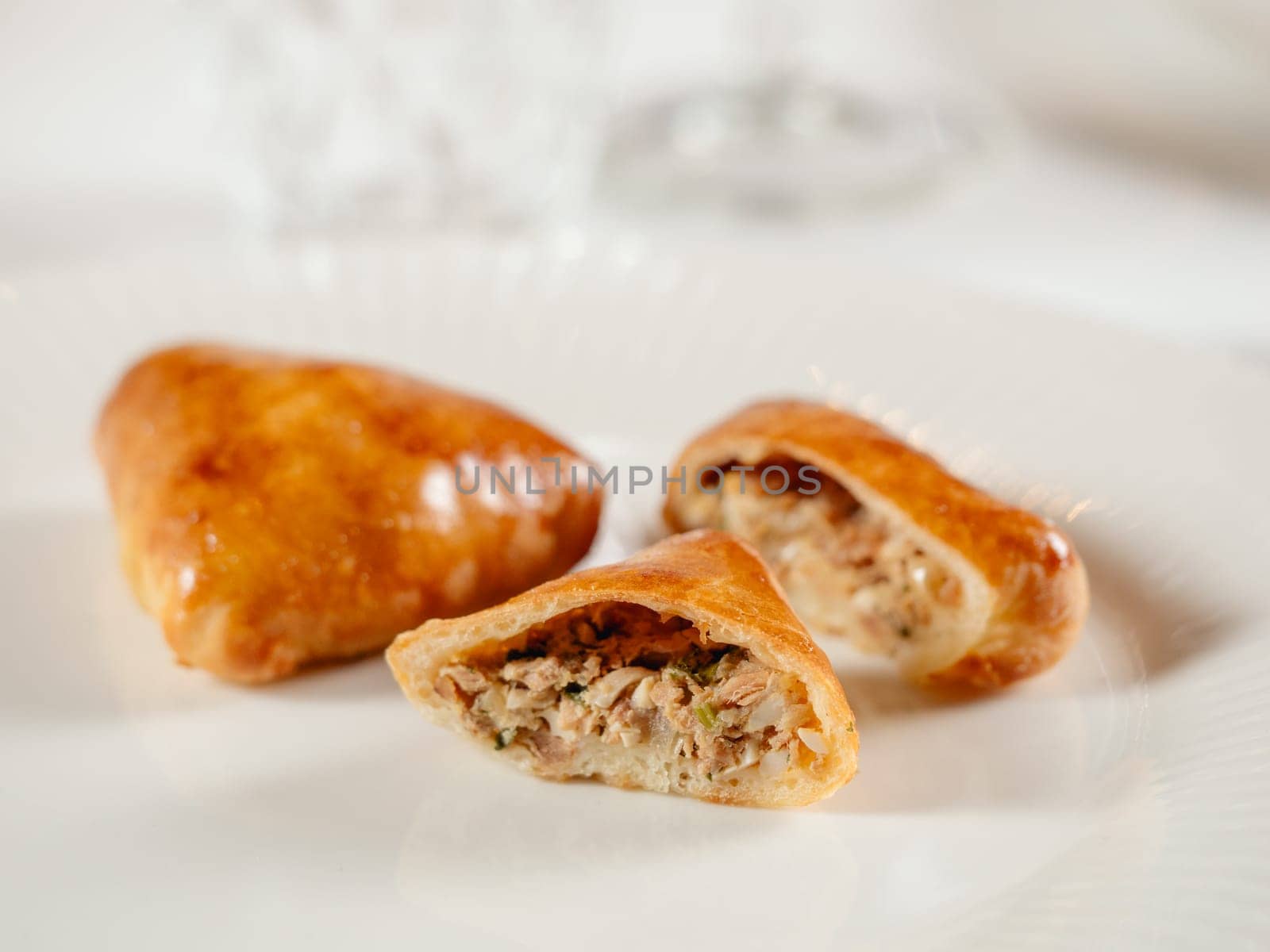 Small russian pies with minced tuna fish Russian Piroshki. Cooked tuna fish hand portioned pies or empanadas cut in half on white plate in elegant restaurant interior. Selective focus, close up.