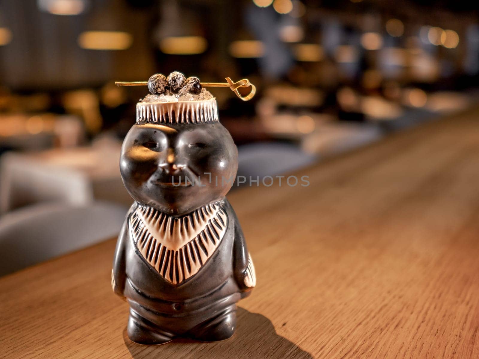 Authentic Tiki Drink Cocktail. Beautiful tropical tiki cocktail on bar counter. Tiki cocktail in monkey mug decorated fig and raspberry on bar in night club or restaurant interior