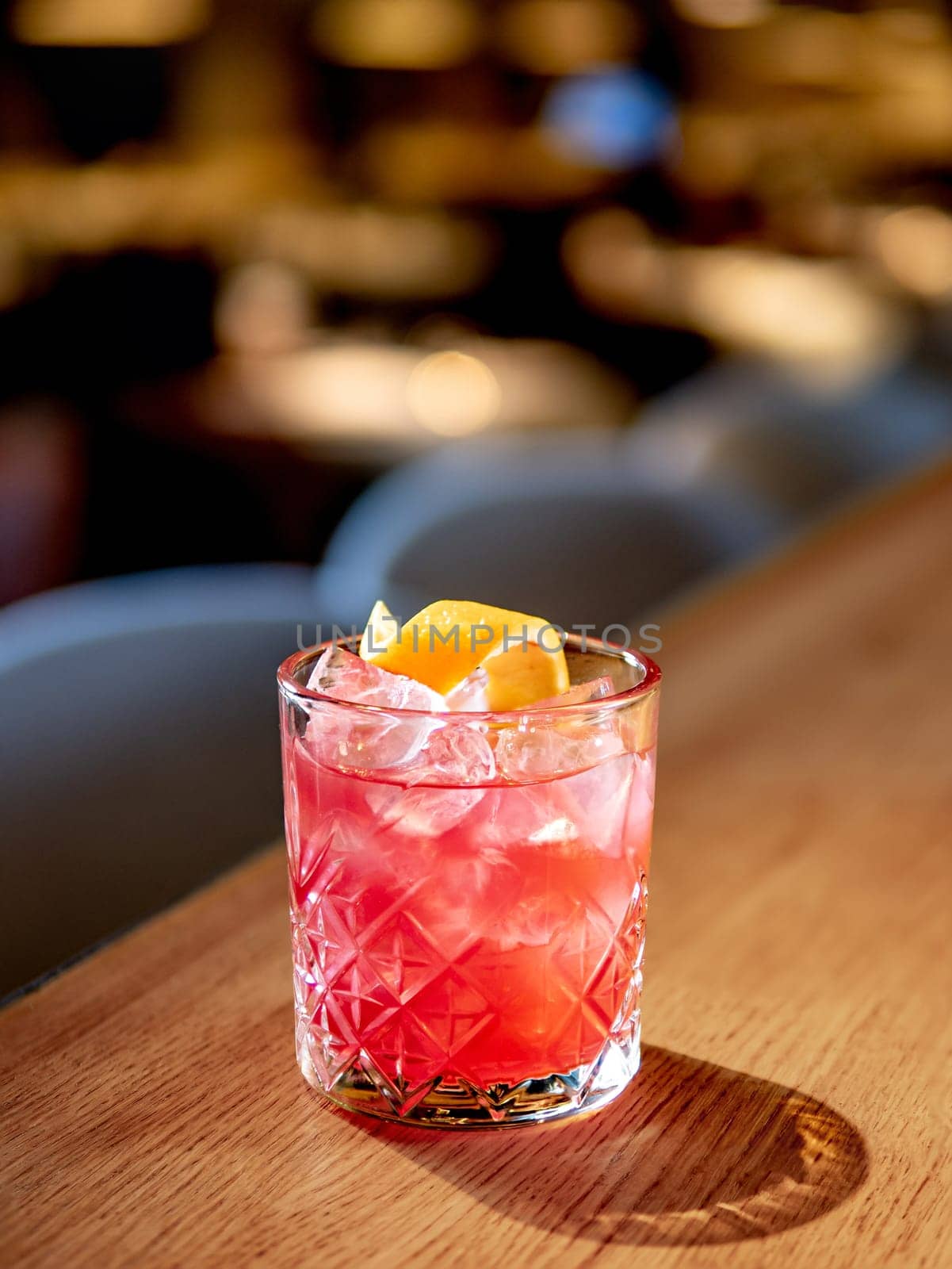 Transparent pink alcohol cocktail with ice, aperol and gin on bar counter in restaurant interior. Alcohol cocktail decorated orange zest spiral. Cold alcoholic cocktail in bar or nightclub. Copy space