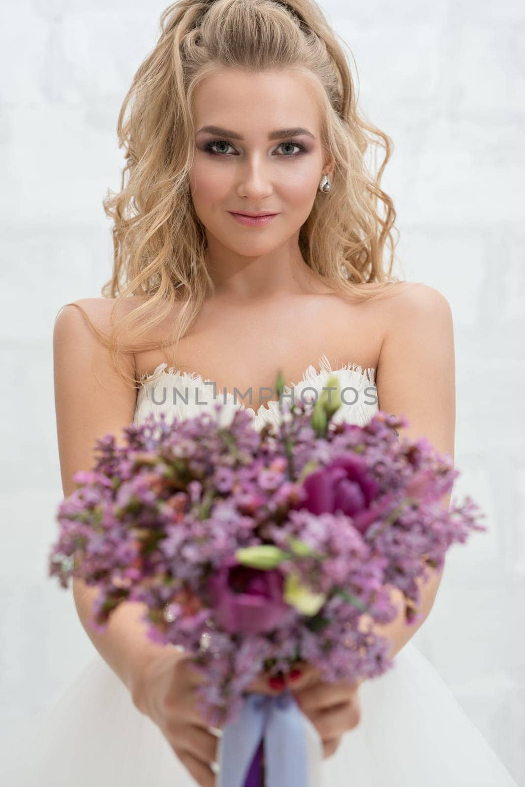 Gorgeous young bride posing in studio with an exquisite pink and violet bouquet