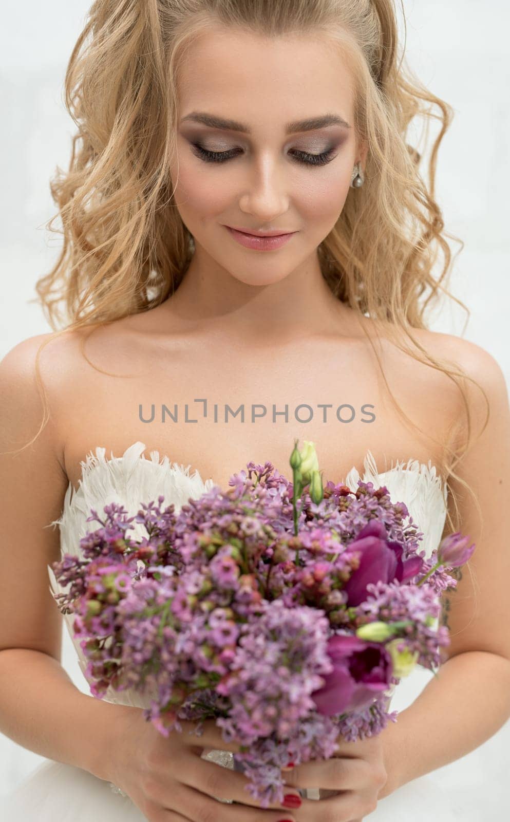 Gorgeous young bride posing in studio admiring her exquisite pink and violet bouquet