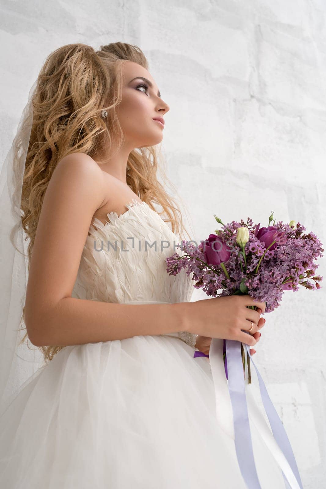 Gorgeous young bride posing in studio with an exquisite pink and violet bouquet shot from below