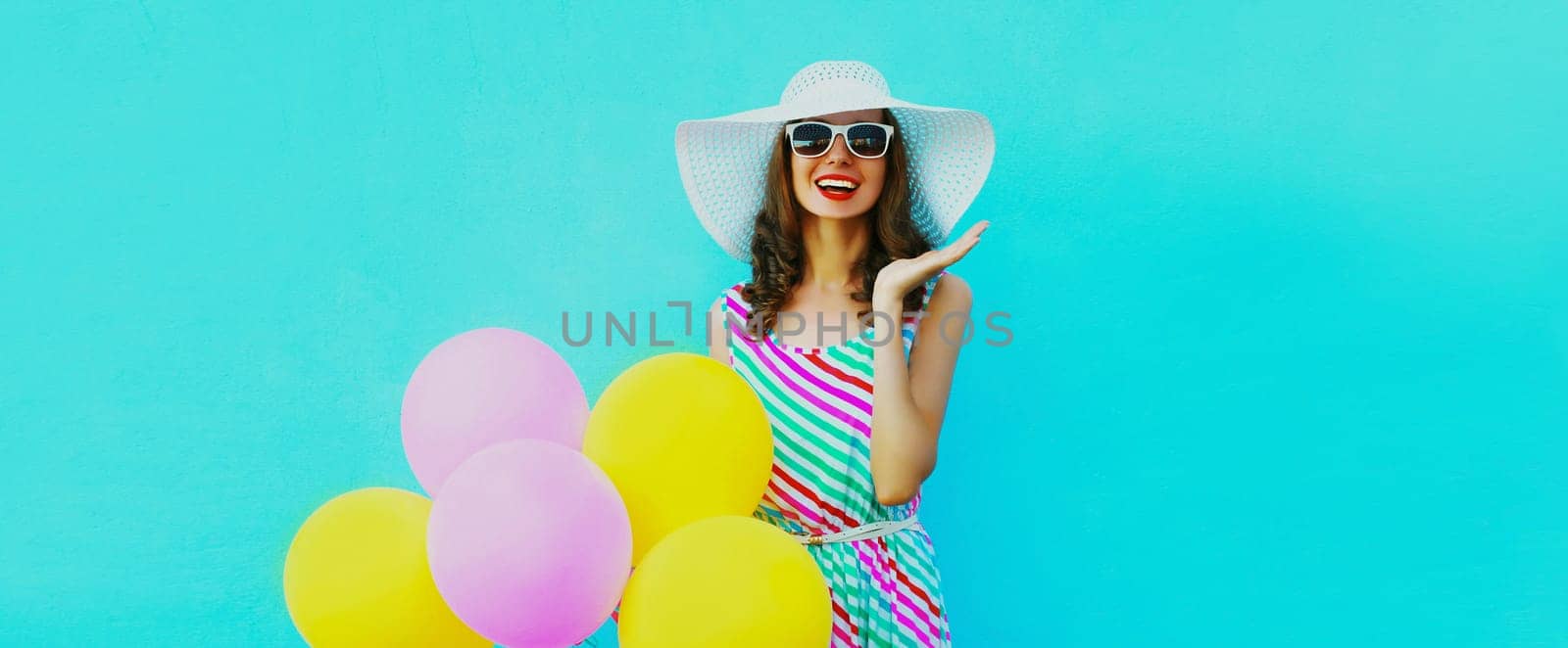 Beautiful happy laughing young woman with bunch of balloons in colorful dress on blue background