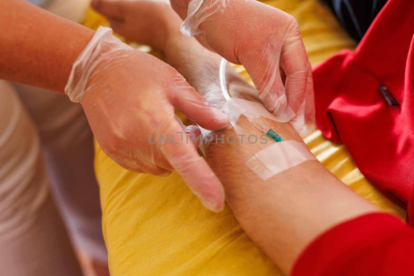 A healthcare professional wearing gloves is preparing to insert an IV into a patient's arm