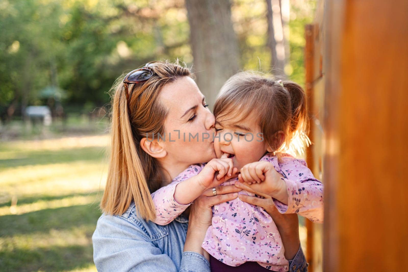 Happy mom kisses her sweet daughter on the playground.
