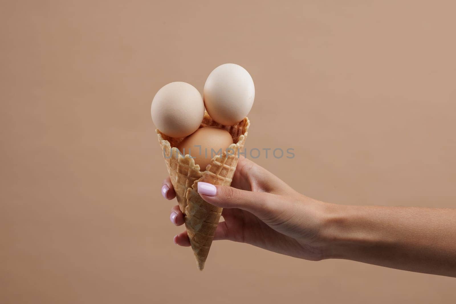 hand holding waffle cone with several chicken eggs on beige background, chicken farm concept, egg market