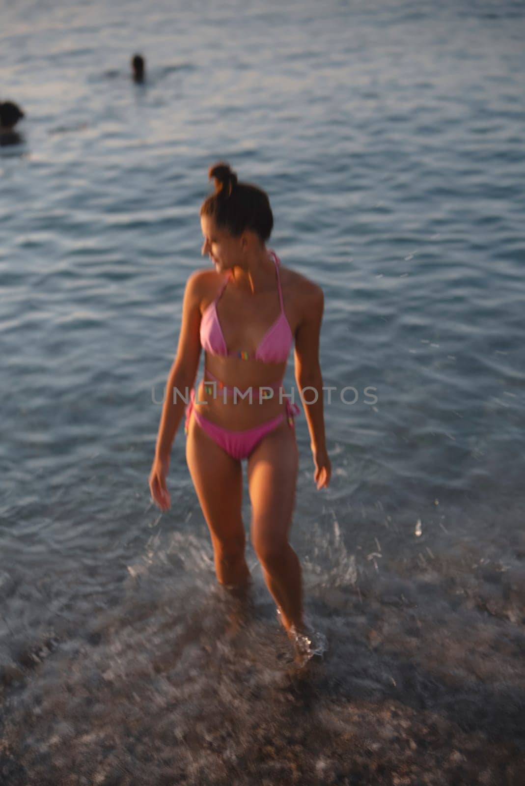 A woman enjoys her time at the beach, playfully walking in shallow water, wearing a stylish pink bikini