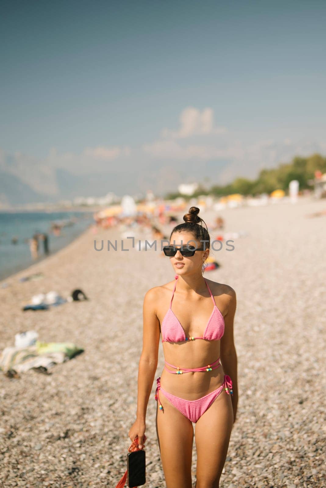 A stylish and fashionable young woman happily enjoys a bright sunny day at the beach while wearing a pink bikini