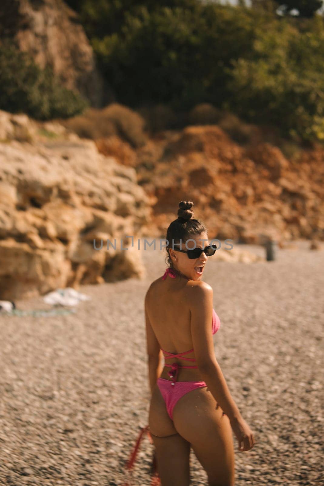 A confident woman strikes a pose in a vibrant pink bikini along the beautiful beach, surrounded by natural beauty