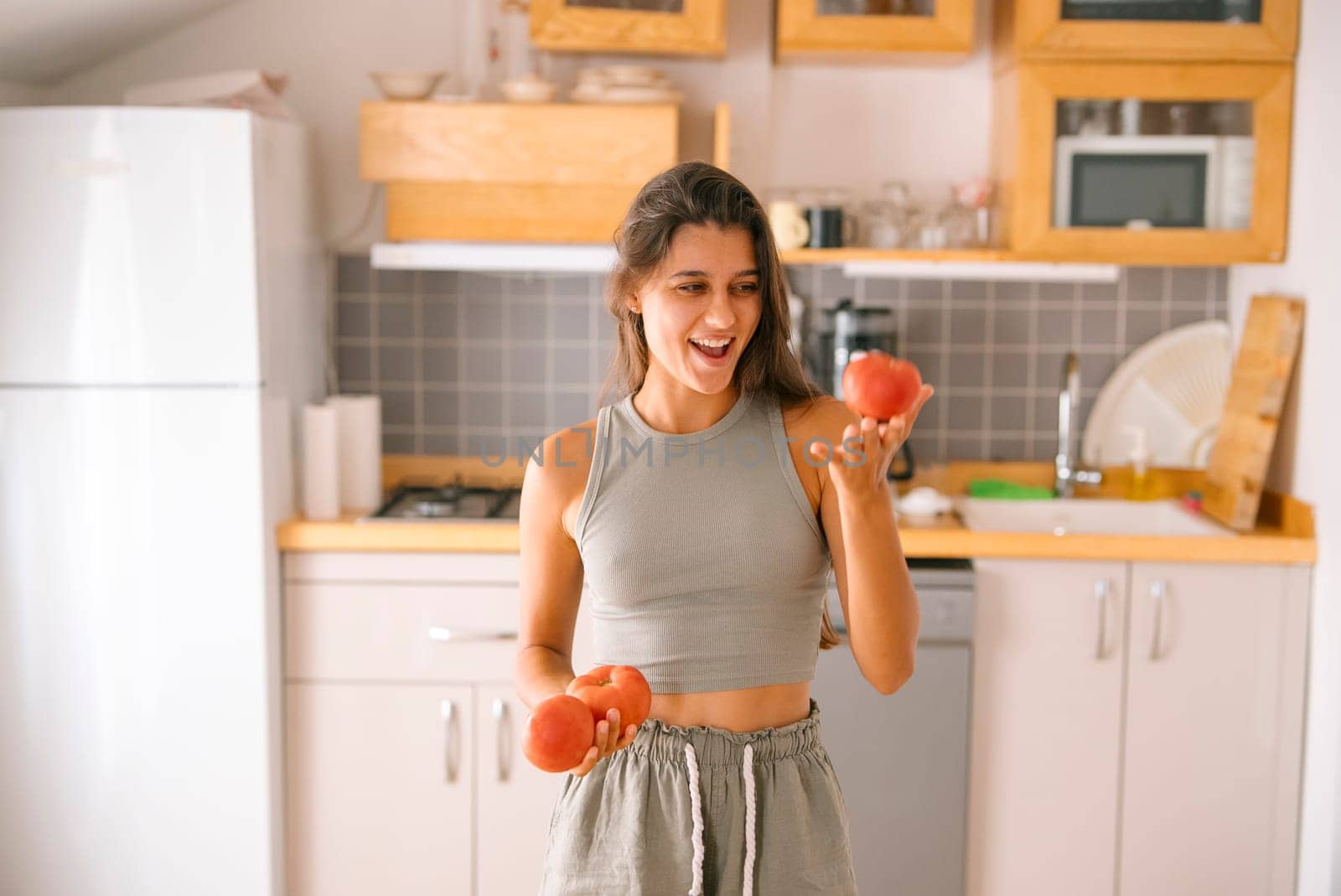 A joyful woman, beaming with happiness, holding fresh tomatoes in a stylish kitchen that exudes healthy living