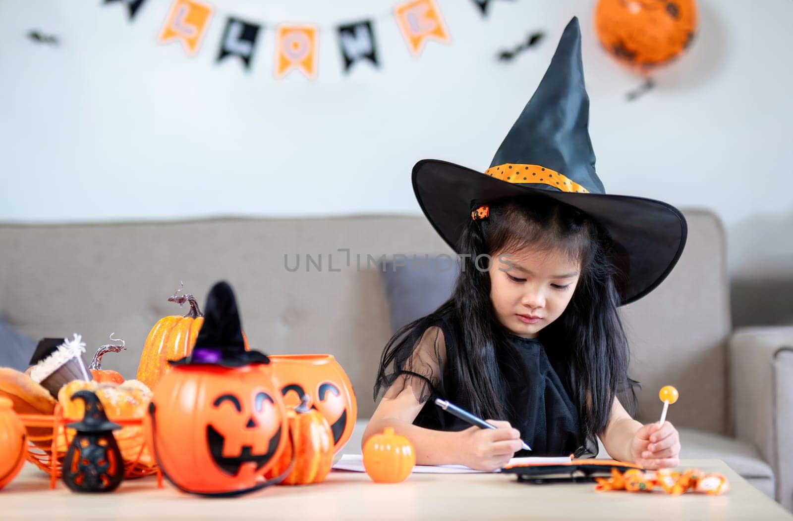 happy halloween. little girl draws a pumpkin and prepares to celebrate halloween at home by wichayada
