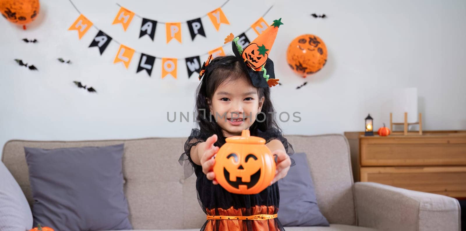 Cute little girl wearing a Halloween costume holding a pumpkin at home with happy eyes. looking at the camera. by wichayada