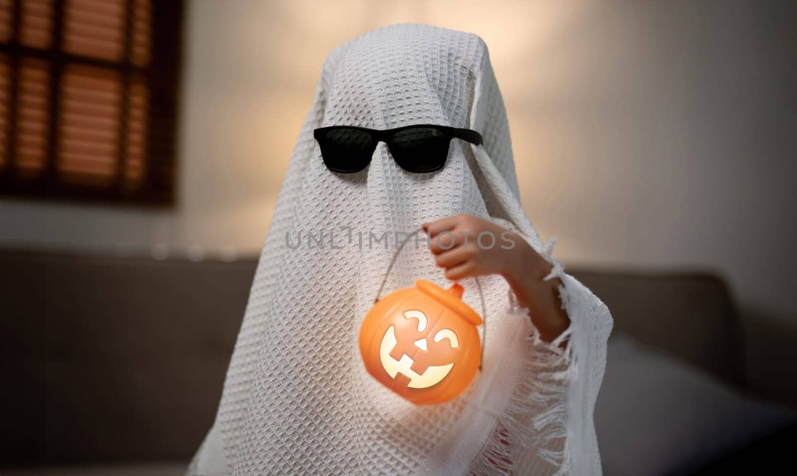 Little children wearing a white scary ghost costume holds a bucket of pumpkins for Halloween..